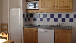 A compact kitchen with wooden cabinets, a microwave, a dishwasher, and a refrigerator. - Bright, well-equipped 3-room apartment with 2 bathrooms and parking space (Orcières-merlette)