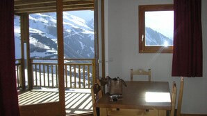 A wooden dining table with chairs, a window with a view of snow-covered mountains, and a wooden balcony with a railing. - Bright, well-equipped 3-room apartment with 2 bathrooms and parking space (Orcières-merlette)