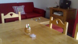 A living room with a wooden table, red sofa, and a television on a wooden stand. - Bright, well-equipped 3-room apartment with 2 bathrooms and parking space (Orcières-merlette)
