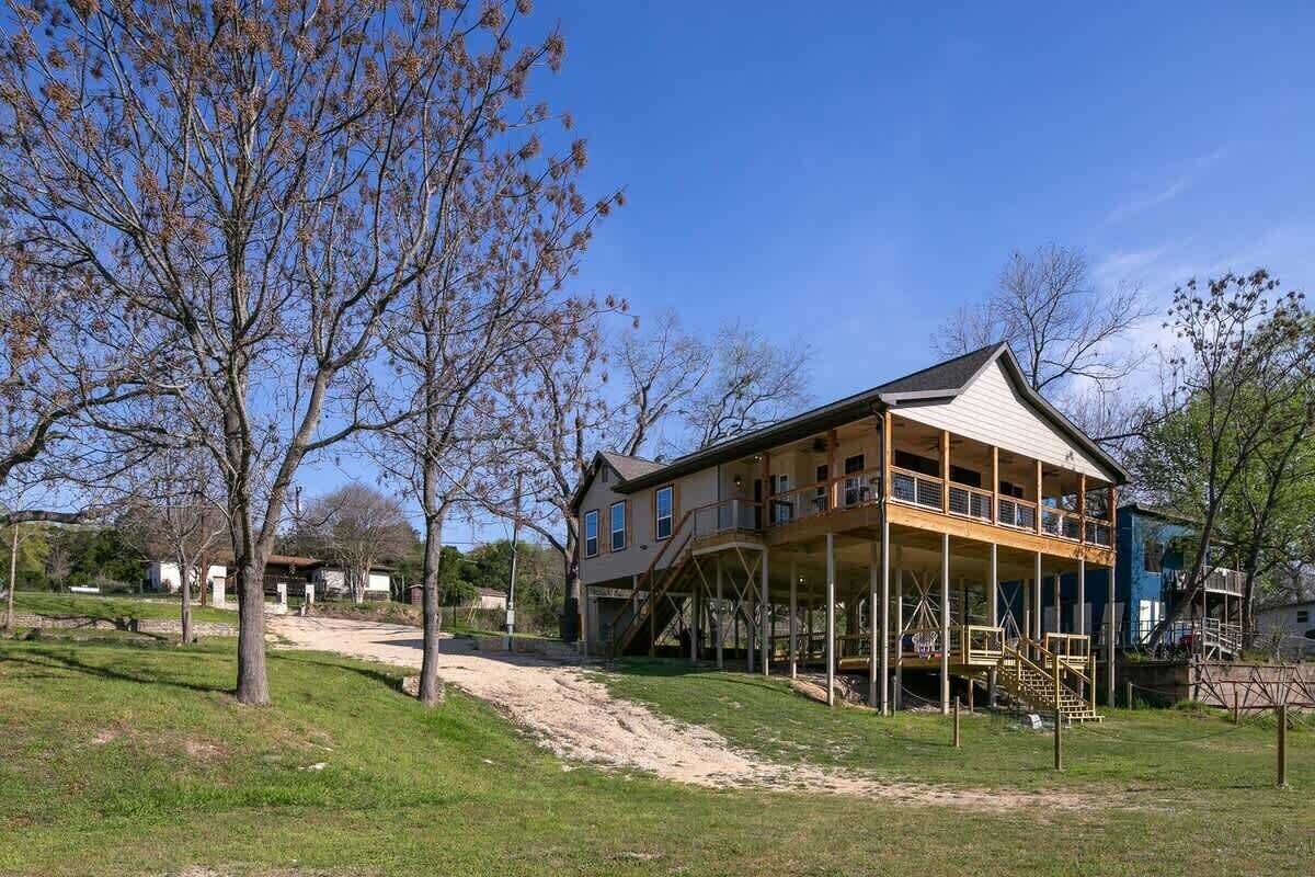 Une maison à deux étages avec un balcon, entourée d’arbres et bordée d’un chemin de terre.