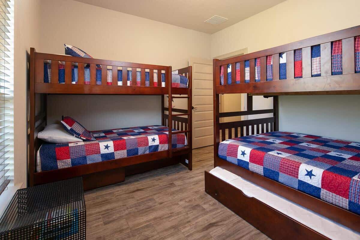 Ein Zimmer mit zwei Etagenbetten, Holz-Kopfteilen, einer kleinen Bank und einem Fenster mit Jalousien.