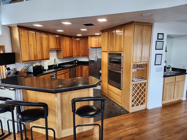 A modern kitchen with wooden cabinets, stainless steel appliances, and a bar area with stools.