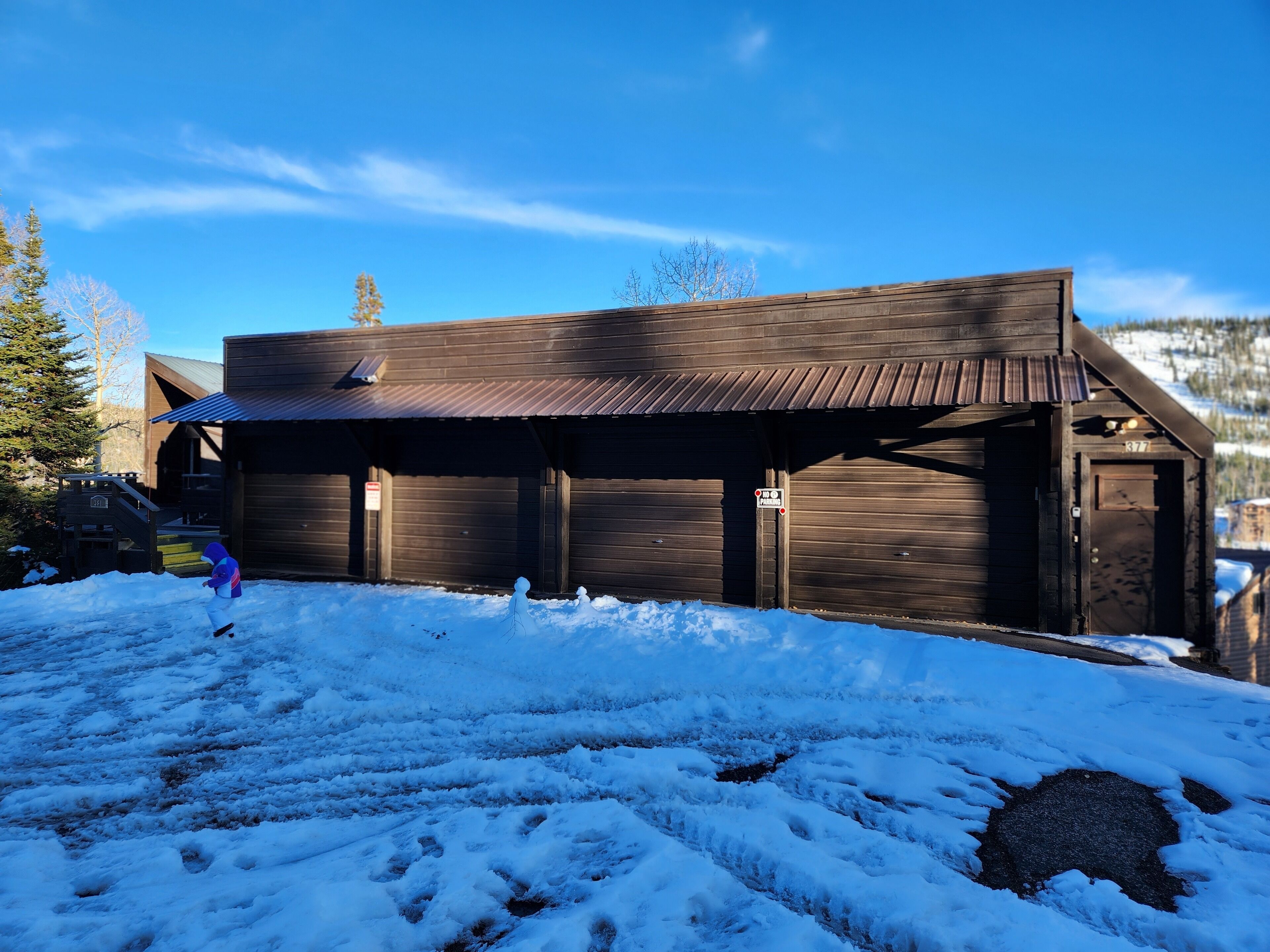 A rustic wooden building with a covered porch, a staircase, and a snow-covered ground.