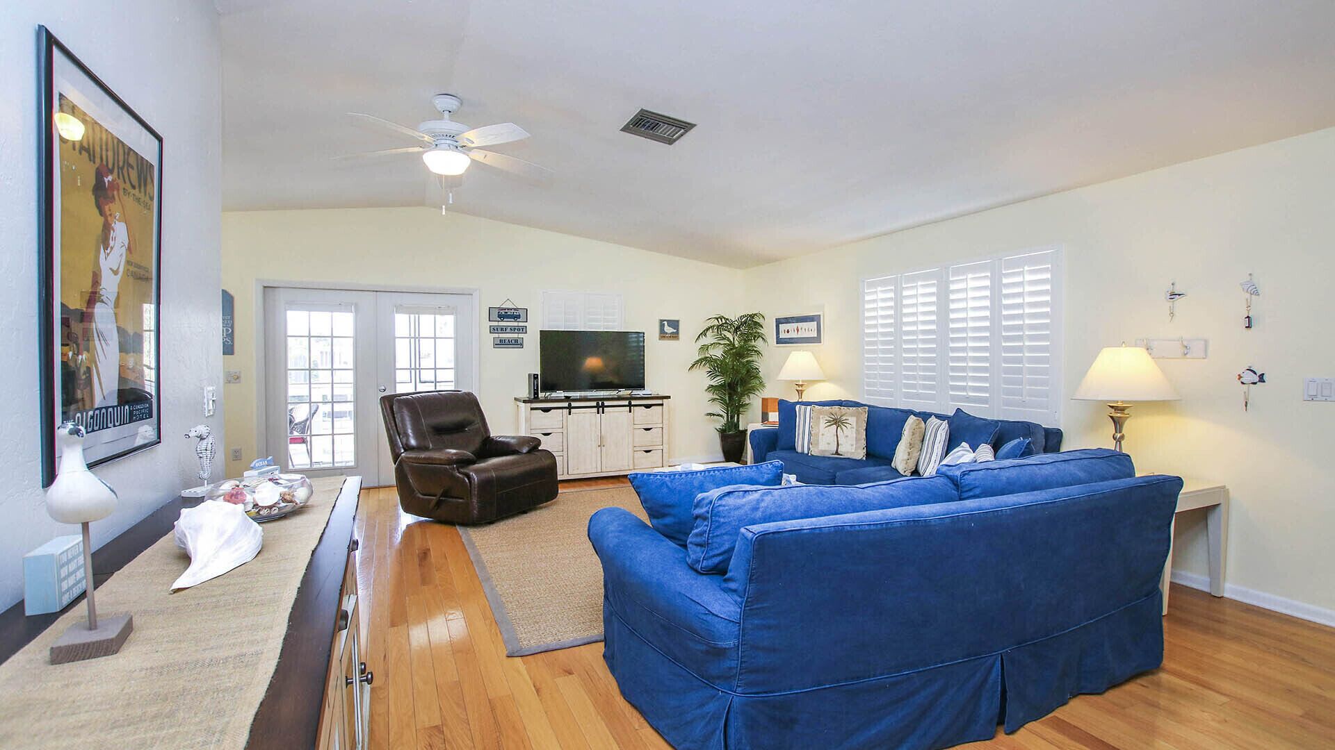 A living room with a blue sofa, a brown leather chair, a TV, and a ceiling fan.