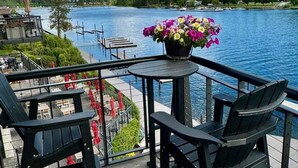 En uteplats med två svarta Adirondack-stolar, ett litet runt bord och en krukväxt med rosa och gula blommor.