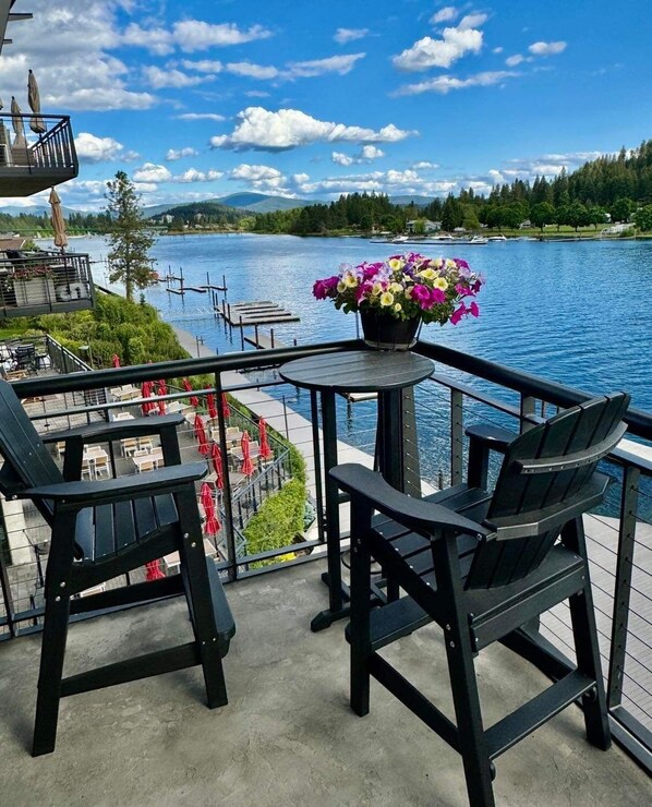 A deck with two black Adirondack chairs, a small round table, and a potted plant with pink and yellow flowers.