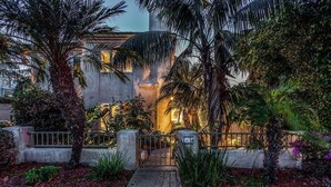 A building with a gated entrance, surrounded by palm trees and various plants.