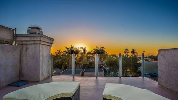 A rooftop terrace with two lounge chairs and a view of the sunset over palm trees.