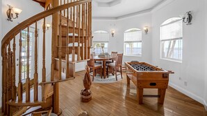 Ein geräumiges Zimmer mit einer Holztreppe, einem Billardtisch und einer Essecke mit einem runden Tisch und Stühlen.