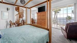 Ein Schlafzimmer mit Himmelbett, Holzmöbeln, einem Fernseher und Blick auf den Ozean.