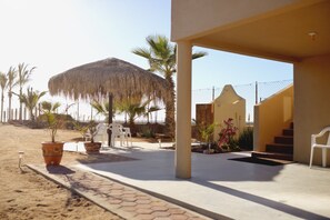 A beachside patio with a thatched umbrella, potted plants, and outdoor seating.