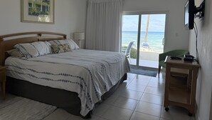 Ein Schlafzimmer mit Bett, Deckenventilator, Fenster mit Vorhängen, Schreibtisch mit Stuhl und Meerblick.