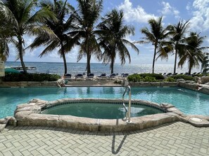 A pool area with lounge chairs, palm trees, and a view of the ocean.