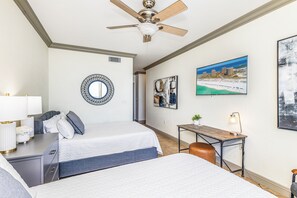 Une chambre d’hôtel avec deux lits, un bureau, un ventilateur de plafond et des œuvres d’art accrochées aux murs.
