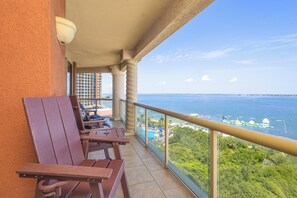 A balcony with wooden chairs and a table, overlooking a body of water with boats and a distant shoreline. - P2-0901 3 Bedroom * Perfect For Large Families (Pensacola Beach)