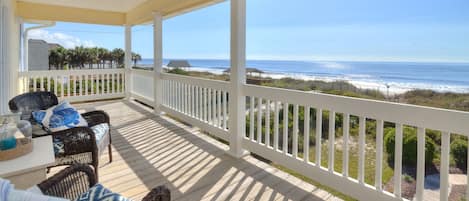 A covered deck with wicker furniture and a view of the beach.