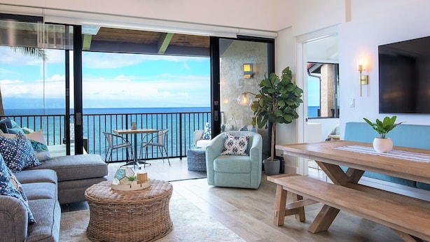 A spacious living area with a balcony overlooking the sea, furnished with a sofa, armchair, and a dining table. - GORGEOUS OCEANFRONT PENTHOUSE  (Lahaina)