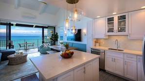 A modern kitchen with a large island, white cabinetry, and a view of the ocean. - GORGEOUS OCEANFRONT PENTHOUSE  (Lahaina)
