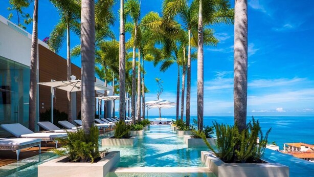 A pool area with lounge chairs and palm trees, overlooking the ocean. - Pier 57 Luxury Escape 2BR, PV’s Best Rooftop! (Puerto Vallarta)