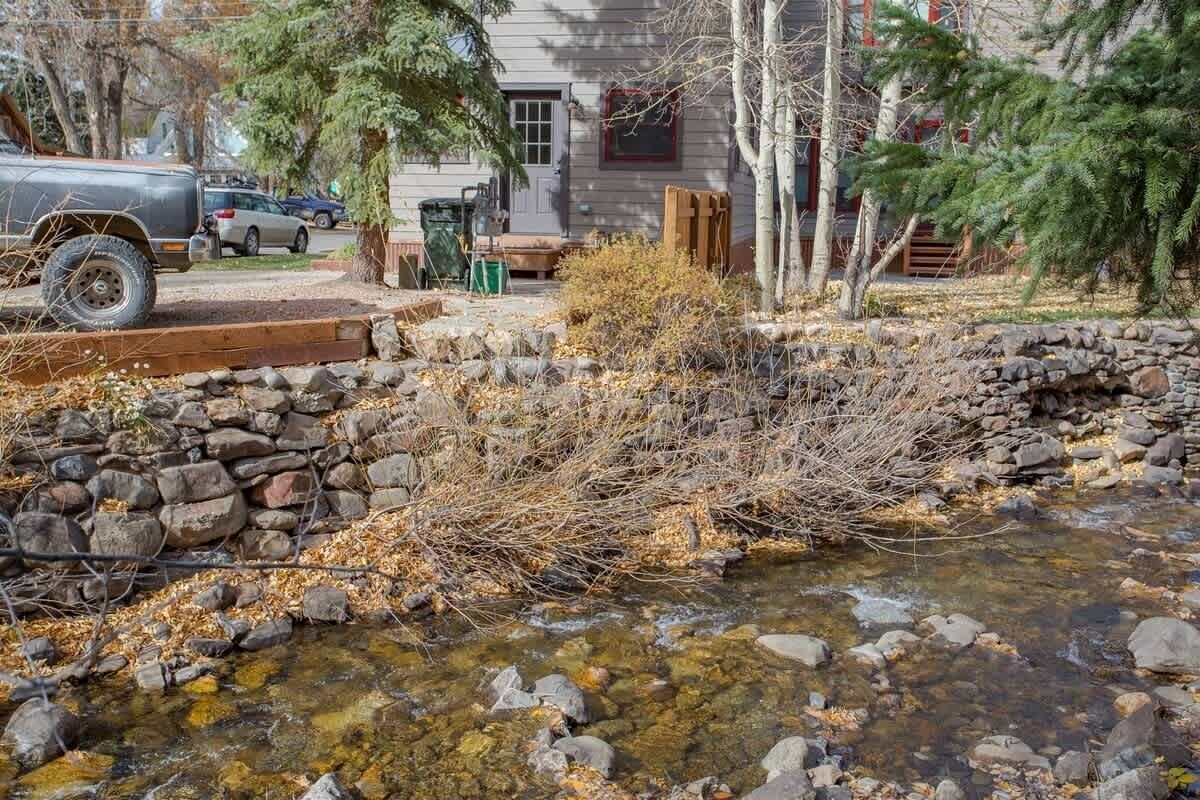 Une cabane rustique avec un ruisseau aux pierres apparentes, un VUS garé et une terrasse en bois.