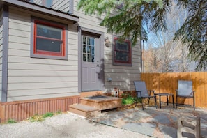 A house with a gray exterior, a gray door, and a small porch with two chairs and a table.