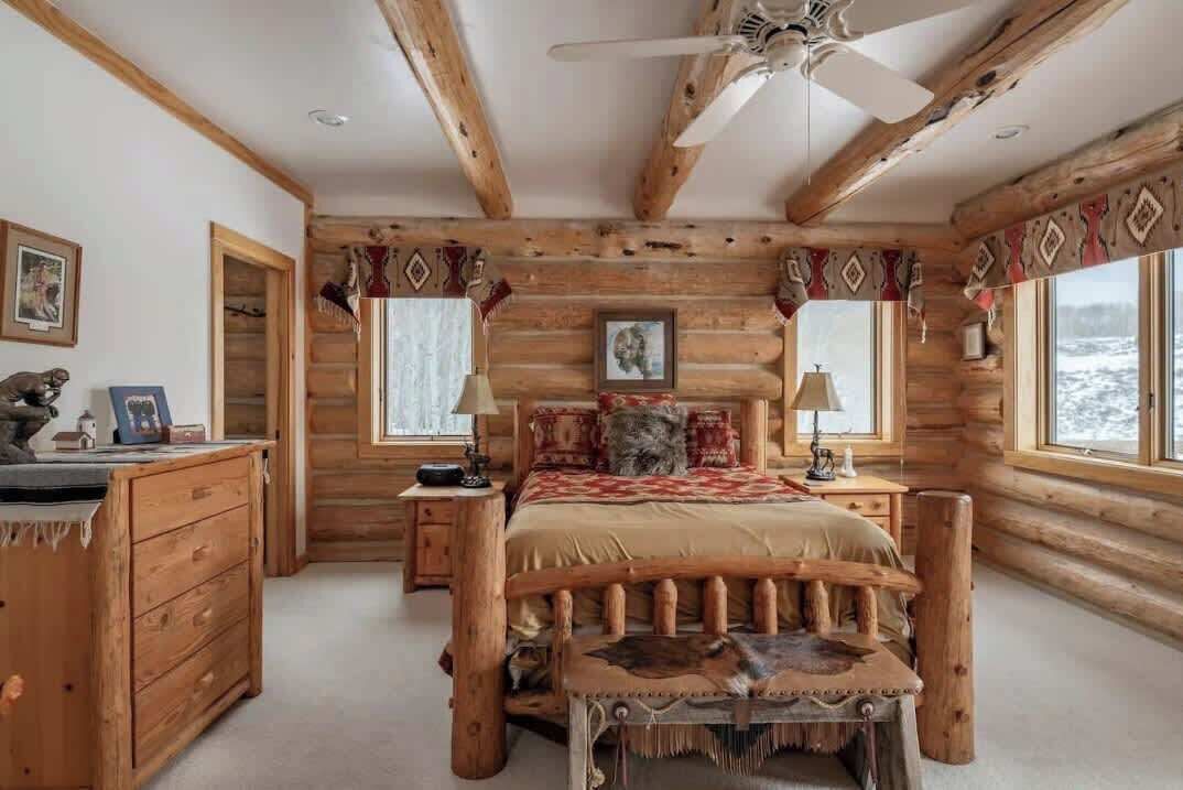 Une chambre située dans une cabane en rondins, avec un lit, une commode en bois et un ventilateur de plafond.