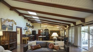 A spacious living room with a dark leather sofa, wooden beams, and a dining area with a chandelier.