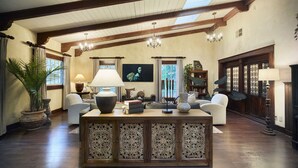 A spacious living room with a high ceiling, wooden beams, a central console table, and a television.