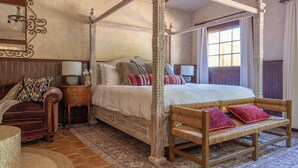 A four-poster bed with a wooden frame and a woven bench beside it.