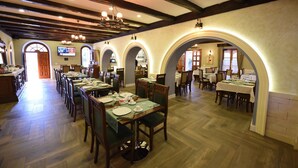 A dining area with multiple tables and chairs, wooden beams on the ceiling, and arched doorways. - Rose Garden Hotel (Shkodër)