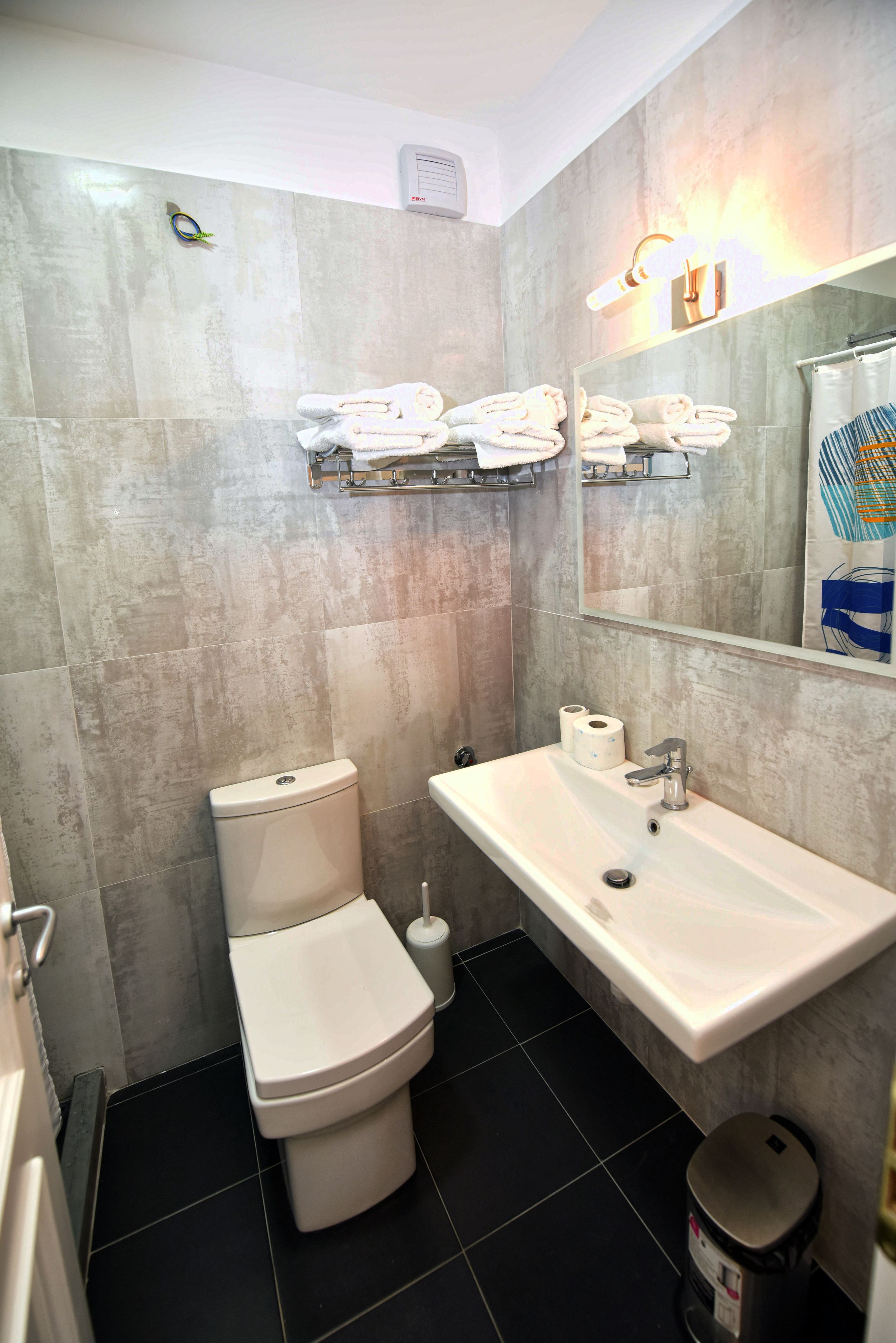 A bathroom with a toilet, sink, and mirror. There are towels on a rack above the sink.