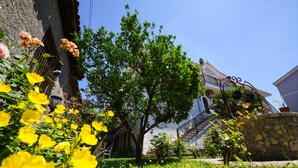 A building with a stone staircase, a tree, and a garden with yellow flowers. - Rose Garden Hotel (Shkodër)