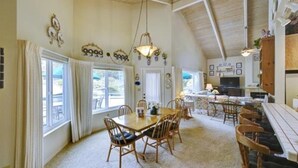 A dining area with a wooden table and chairs, a kitchen in the background, and a high ceiling with exposed beams. - Rio Del Mar Aptos-two blocks to the Sand, Ocean, Store, Restaurant, Coffee shop (Aptos)