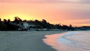 A beach with a calm sea, a sunset, and a rocky coastline with buildings. - Rio Del Mar Aptos-two blocks to the Sand, Ocean, Store, Restaurant, Coffee shop (Aptos)