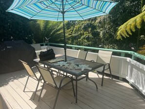 En overdækket terrasse med bord og stole, grill og en stribet parasol.