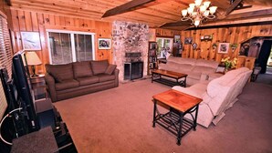 Ein gemütliches Wohnzimmer mit Kamin aus Stein, Holzwänden und einer Kristallleuchter.