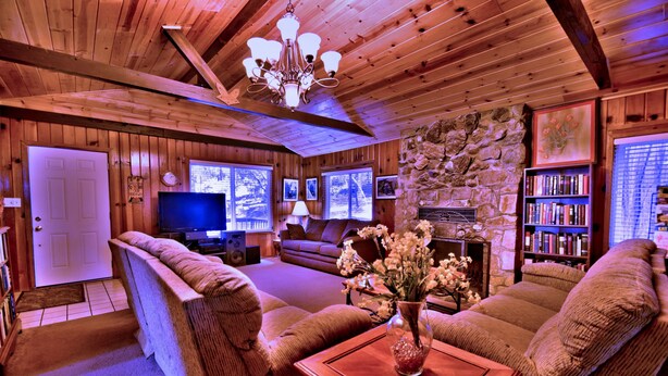 Ein gemütliches Blockhaus-Interieur mit Holzwänden, einem Steinkamin, einer Couch, einem Couchtisch und einem Bücherregal.