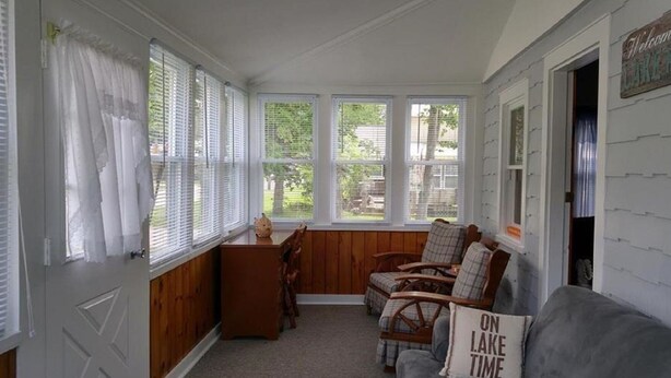 Un solarium con ventanas amplias, un banco de madera y un letrero que dice "Welcome to Lake House".