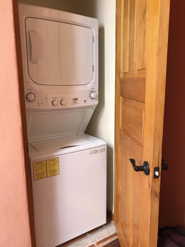 A compact, white laundry machine with a front-loading door, located in a corner next to a wooden door.