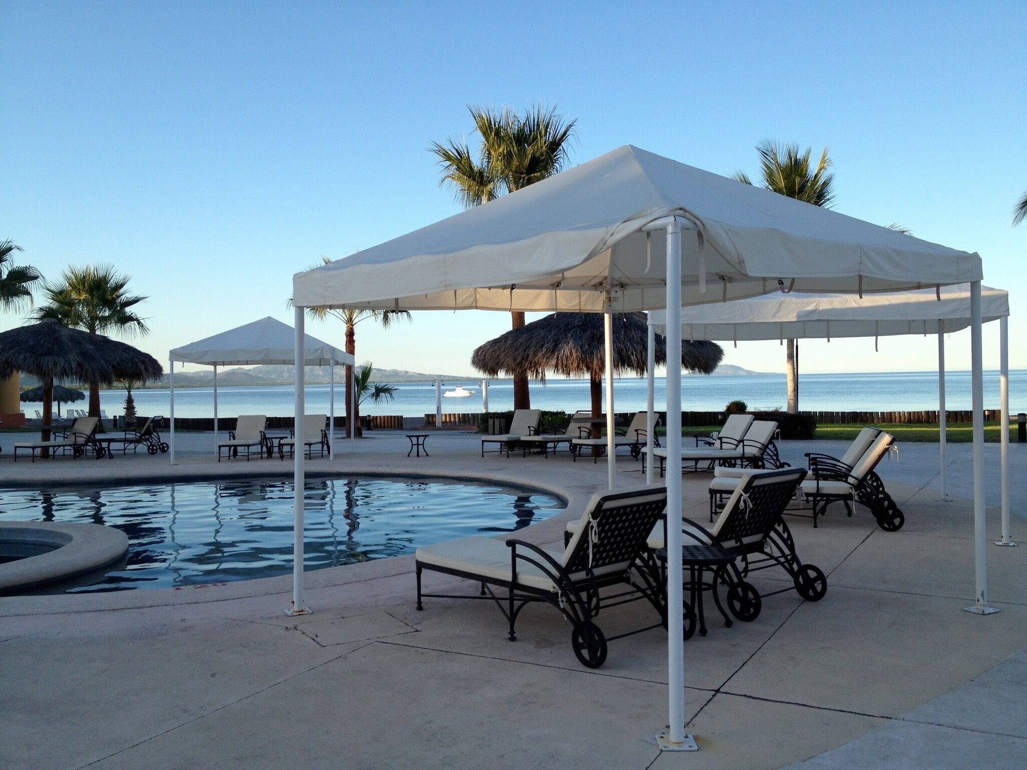 A poolside area with lounge chairs and umbrellas, a pool, and a view of the sea.