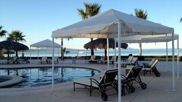 A poolside area with lounge chairs and umbrellas, a pool, and a view of the sea.