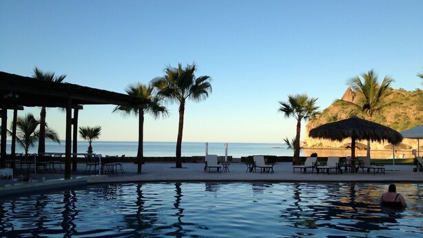 A poolside area with lounge chairs and umbrellas, overlooking a beach and ocean.