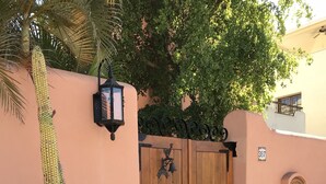 A wooden gate with a bell and a mailbox, surrounded by cacti and rocks.