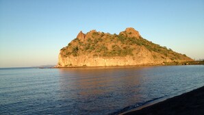 A coastal landscape with a prominent rocky hill and calm sea.