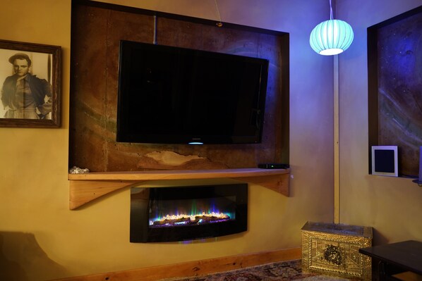 Una sala de estar con un televisor de pantalla plana montado, una chimenea y una lámpara decorativa.