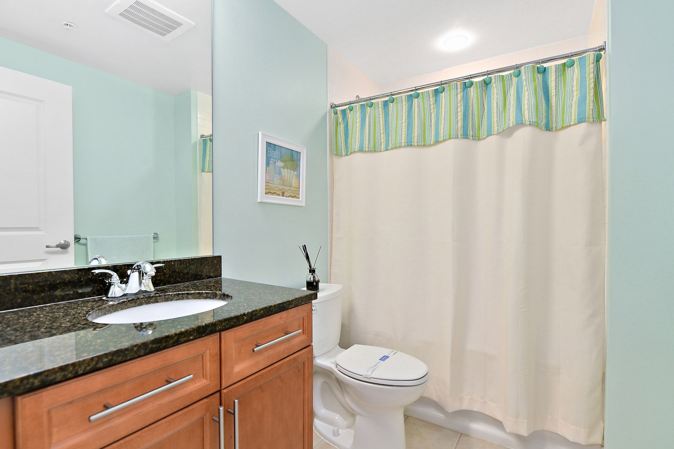 A bathroom with a sink, mirror, toilet, and shower curtain.