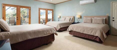 A bedroom with two beds, a ceiling fan, an air conditioning unit, and a view through the glass doors.