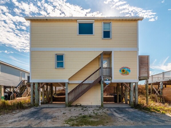 A two-story beach house with a wooden deck and a staircase leading to the entrance. - Sunflower Beach House | Oceanfront + Walk to Beach (Surf City)