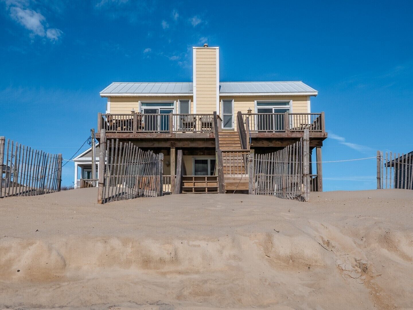 A two-story beach house with a balcony, a front porch, and a sandy driveway.