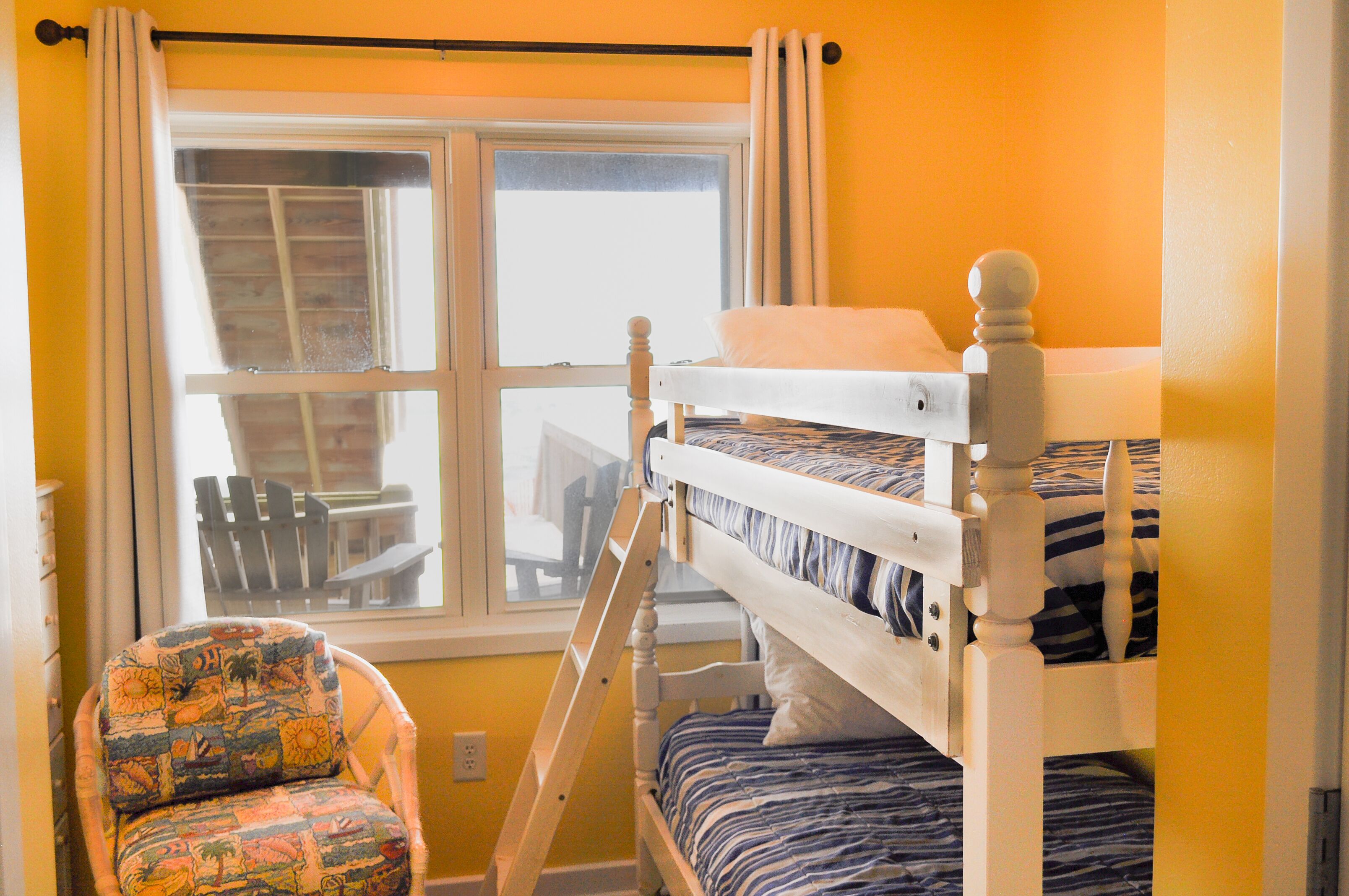 A bunk bed room with a window, a chair, and a ladder.